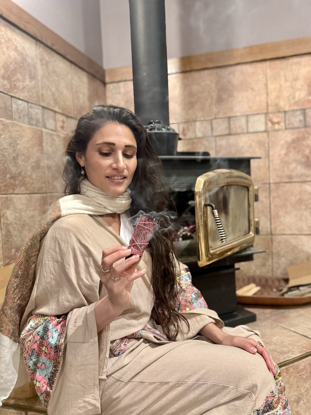 Amira Attar holding a sage smudge stick, a quiet ritual moment